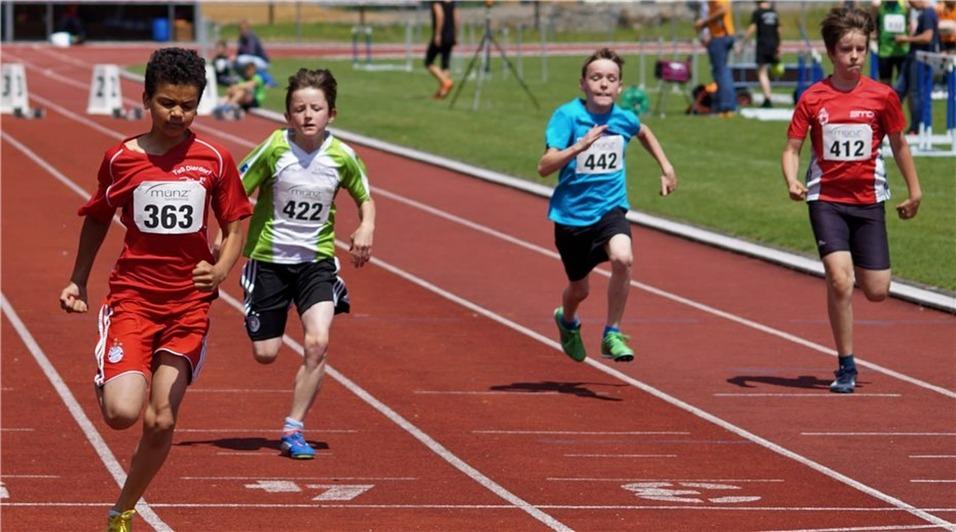 Vier Kinder in Sportbekleidung sprinten auf einer roten Laufbahn während eines Leichtathletikwettbewerbs.