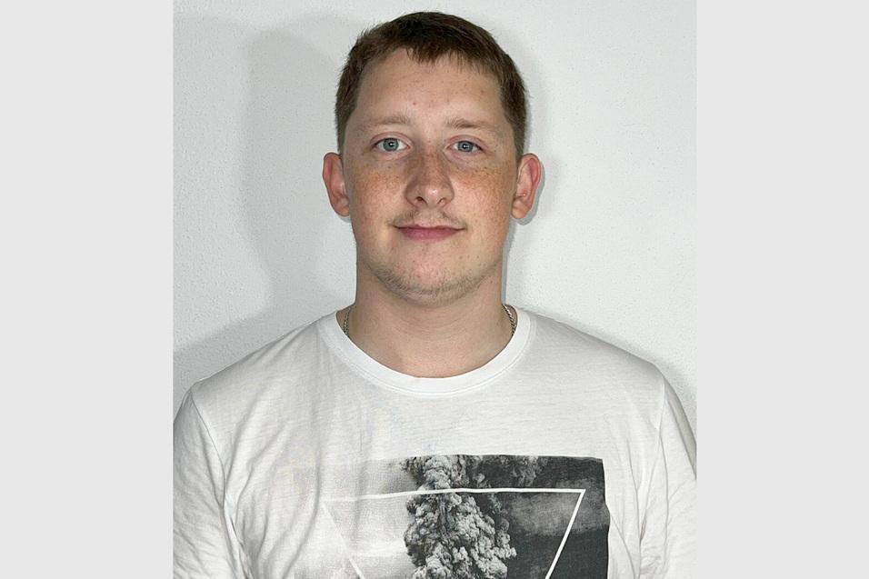 Porträt eines jungen Mannes mit kurzem, hellbraunem Haar und einem weißen T-Shirt mit grafischem Druck vor neutralem Hintergrund.