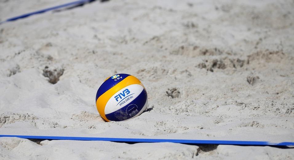 Nahaufnahme eines Beachvolleyballs auf hellem Sand, daneben ein blauer Markierungsstreifen.