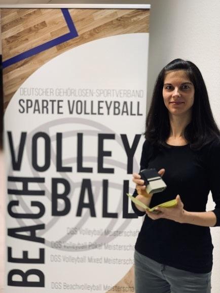 Frau hält einen Preis in der Hand, vor einem Banner des Deutschen Gehörlosen-Sportverbands mit dem Thema Volleyball.