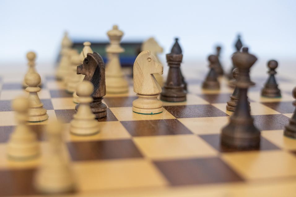 Nahaufnahme eines Schachbretts mit Holzfiguren, darunter zwei Pferde und verschiedene andere Figuren in verschiedenen Farben.